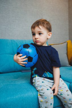 İki yaşında küçük bir çocuk elinde bir topla kanepede oturuyordu. Gelişmiş duygusal bir çocuk evde topla oynuyor.