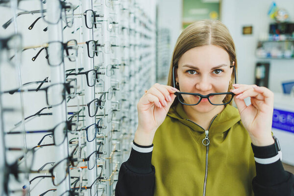 A young woman chooses glasses for vision correction. Ophthalmology shop with glasses to improve eyesight.