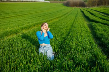Gülümseyen genç bir kadın yeşil çimlerin üzerinde geniş bir alanda oturuyor..