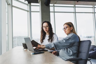 Ofis odasında oturmuş dizüstü bilgisayarla çalışan kendine güvenen iki güzel genç kadın. Modern bir ofisteki meslektaşların işi..