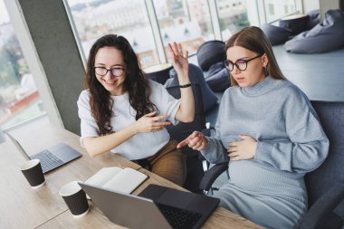 Ofis odasında oturmuş dizüstü bilgisayarla çalışan kendine güvenen iki güzel genç kadın. Modern bir ofisteki meslektaşların işi..
