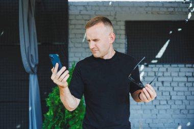 Şirin bir genç adam elinde dizüstü bilgisayarla bir kafede bir terasta duruyor ve telefonla konuşuyor. Çevrimiçi çalış, serbest çalışan. Çevrimiçi uzak yaz işi.