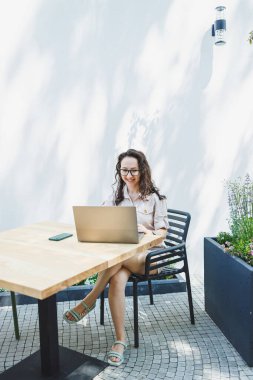 Bir bayan öğrenci bir kafede yaz terasında oturur ve bir dizüstü bilgisayarda çalışır. Serbest çalışan bir kadın, yazlık bir kafede otururken uzaktan çalışıyor. Uzak çalışma