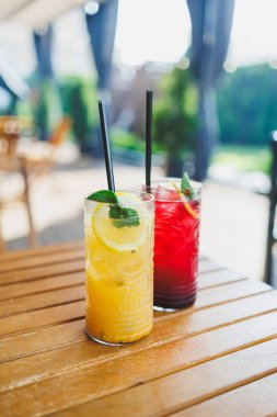 Tahta bir masada iki bardak ferahlatıcı meyve limonatası standı. Yaz meşrubatları