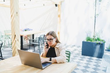 Dışarıdaki kafe masasında dizüstü bilgisayarla oturan gülümseyen kadın, telefonla konuşan ve kahve içen, bardaklı gülümseyen kadın kafede gezmekten ya da internetten ders çalışmaktan zevk alan kadın.