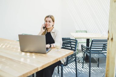 Genç, mutlu bir kadın açık kafeteryada oturuyor ve telefonda bir fincan kahveyle konuşuyor. Gülümseyen bir kadın kafede gezmekten zevk alıyor. Ya da bilgisayarla internetten ders çalışıyor.