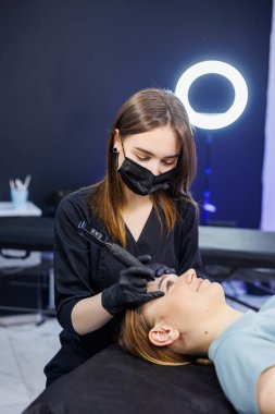 Kalıcı makyaj aleti olan profesyonel bir kadın makyöz. Genç bir makyajcı kalıcı kaş makyajı yapar.