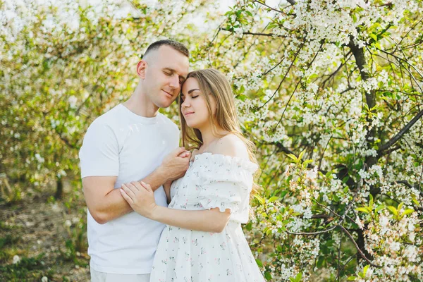 Romantik bir yerde hamilelik bekleyen genç ve güzel bir çift. Çiçek açan bir elma bahçesi. Bahçede yürürken eğlenen mutlu çift. Bir erkek bir kadının elini tutar.
