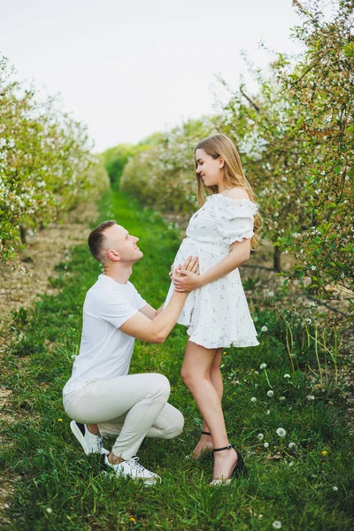 Beautiful young couple in spring garden. Beauty lifestyle family concept. A happy mother is expecting a baby. A happy young couple in a blooming garden