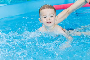 2 yaşındaki bir çocuk bir koçla havuzda yüzmeyi öğreniyor. Çocuklar için yüzme dersleri. Çocuklar için yüzme okulu. Çocuklar için eğitici yüzme dersleri