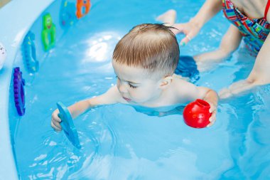 2 yaşında küçük bir çocuk havuzda yüzmeyi öğreniyor. Küçük çocuklar için yüzme dersleri. Çocuklar için yüzme okulu.