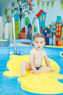 2 yaşında küçük bir çocuk havuzda yüzmeyi öğreniyor. Küçük çocuklar için yüzme dersleri. Çocuklar için yüzme okulu.