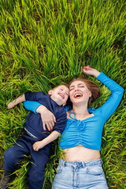 Genç bir anne ve oğlu yeşil çimlerin üzerinde yatıyor. Anne ve çocuğun aile ilişkileri. Mutlu bir aile.