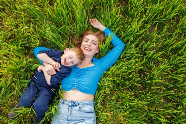 Genç bir anne ve oğlu yeşil çimlerin üzerinde yatıyor. Anne ve çocuğun aile ilişkileri. Mutlu bir aile.