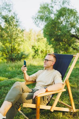 Şehir parkındaki bankta oturan bir adam akıllı telefondan konuşuyor. Genç bir adam haberleri okuyor, cep telefonuna mesaj yazıyor. Doğada eğlence, tatilde uzaktan çalışma.
