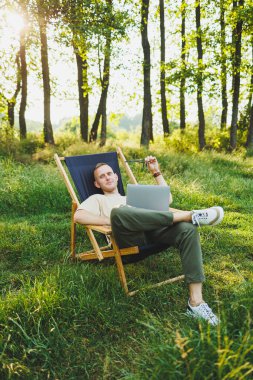 Şehir parkındaki bankta oturan bir adam dizüstü bilgisayarda çalışıyor. Genç bir adam haberleri okuyor, dizüstü bilgisayarına bir mesaj yazıyor. Doğada eğlence, tatilde uzaktan çalışma.