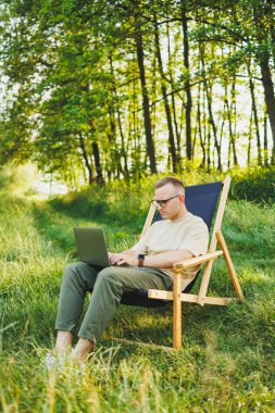 Şehir parkındaki bankta oturan bir adam dizüstü bilgisayarda çalışıyor. Genç bir adam haberleri okuyor, dizüstü bilgisayarına bir mesaj yazıyor. Doğada eğlence, tatilde uzaktan çalışma.