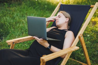 Sevimli hamile bir kadın parkta oturuyor ve uzaktan bilgisayarla çalışıyor. Doğum izninde online iş. Modern hamile kadın