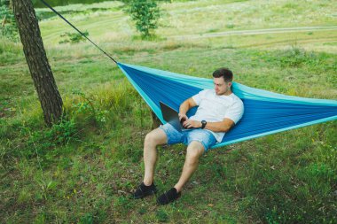 Hamakta dinlenen yakışıklı yetişkin bir adam. Gün boyu dışarıda dolaşırken dizüstü bilgisayarda çalışıyor. Uzak çalışma ile doğada dinlenme