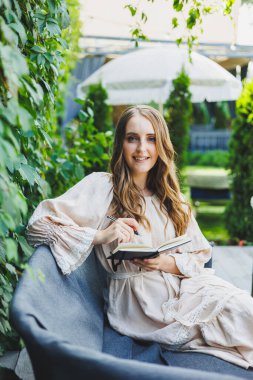 Yazlık terasta dizüstü bilgisayarda bağımsız çalışan bir kadın. Elbise giymiş bir iş kadını su içer ve dizüstü bilgisayarda çalışır.