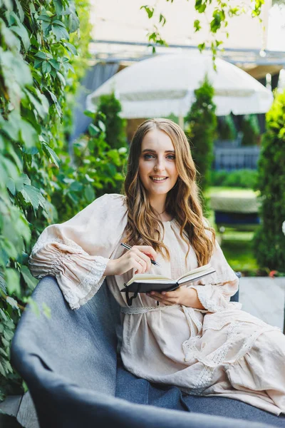 Yazlık terasta dizüstü bilgisayarda bağımsız çalışan bir kadın. Elbise giymiş bir iş kadını su içer ve dizüstü bilgisayarda çalışır.