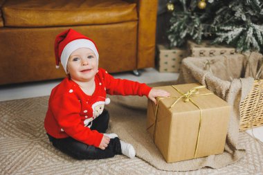 1 yaşındaki küçük bir çocuk bir sepetin içinde Noel ağacının arka planında oturuyor. Yeni yıl rüzgarında bir çocuk Noel ağacının yanında