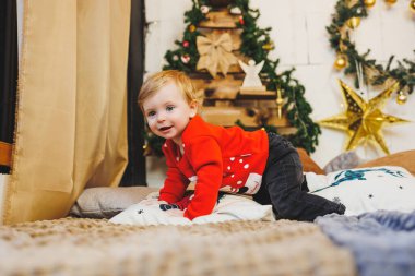 Noel ağacının yanında bir yaşında küçük bir çocuk. Yeni yıl için bir çocuk fotoğrafı fikri. Stüdyo Yeni Yıl dekorasyonu. Noel hediyeleri, kırmızı çocuk kostümleri.