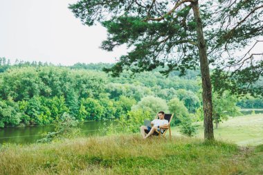 Yakışıklı adamın doğada sandalyede yatıp dizüstü bilgisayarla çalışmasını, tek başına dinlenmesini düşünceli bir şekilde yukarı bakmasını görmek. Kırsalda geziye çıkmış bir adam. İnsanların yaşam tarzı kavramı