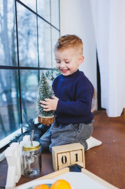 Yeni yılda 2 yaşında bir çocuk pencerenin kenarında oturur. Evde yeni yıl atmosferi. Çocuk yeni yılı bekliyor..