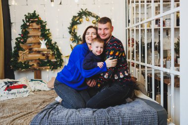 Yeni yıl mekanlarında çocuklu mutlu aile çifti. Aile çevresinde yeni yılın şenlik havası. Yatak odasında Noel süsleri var. Evde yeni yıl. Evde Noel süslemeleri