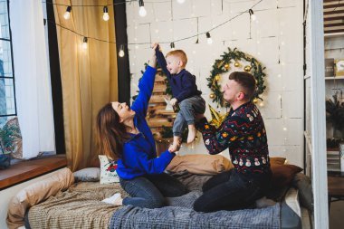 Yeni yıl mekanlarında çocuklu mutlu aile çifti. Aile çevresinde yeni yılın şenlik havası. Yatak odasında Noel süsleri var. Evde yeni yıl. Evde Noel süslemeleri