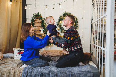 Küçük çocuklu neşeli bir genç aile evdeki Noel ağacının yanında dinleniyor. Evde Noel süsü olan aile çifti. Noel, Yeni Yıl - kutlama zamanı