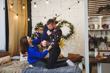 Küçük çocuklu neşeli bir genç aile evdeki Noel ağacının yanında dinleniyor. Evde Noel süsü olan aile çifti. Noel, Yeni Yıl - kutlama zamanı