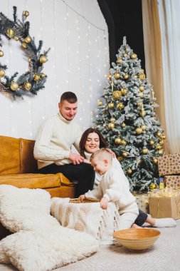 Küçük çocuklu neşeli bir genç aile evdeki Noel ağacının yanında dinleniyor. Evde Noel süsü olan aile çifti. Noel, Yeni Yıl - kutlama zamanı