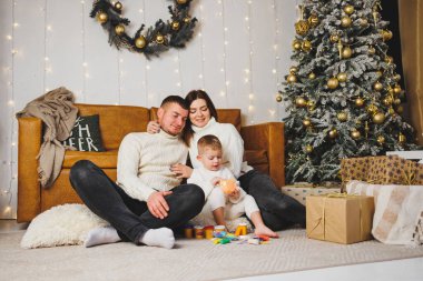 Küçük bir çocuklu mutlu bir genç aile Noel ağacının yanında yeni yılı evde kutluyor. Aileyle Noel, Yeni Yıl - kutlama zamanı.