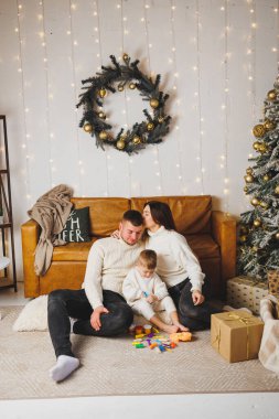 Küçük bir çocuklu mutlu bir genç aile Noel ağacının yanında yeni yılı evde kutluyor. Aileyle Noel, Yeni Yıl - kutlama zamanı.