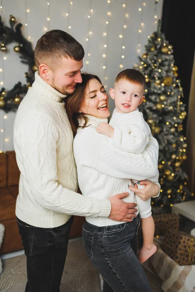 stock image A happy young family with a small child is celebrating the New Year at home near the Christmas tree. Christmas with the family, New Year - time to celebrate.