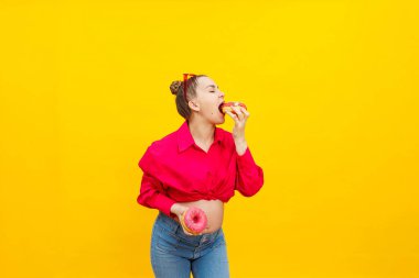 Hamile kadın sarı arka planda tatlı çörekler yiyor. Pembe gömlekli ve gözlüklü hamile bir kadın tatlı bir pasta yiyor. Hamilelik süresince zararlı yiyecekler.