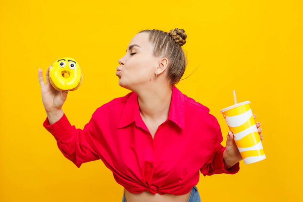 A smiling pregnant woman in a pink shirt is eating a sweet cake and drinking a sweet drink. Happy pregnant woman eats unhealthy sweet donuts.