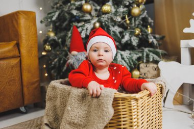 Noel ağacının yanında bir yaşında küçük bir çocuk. Yeni yıl için bir çocuk fotoğrafı fikri. Stüdyo Yeni Yıl dekorasyonu. Noel hediyeleri, kırmızı çocuk kostümleri.