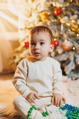 1 yaşında, Noel ağacının yanında, ağacın altında, yerde oturan tatlı bir çocuk. Tatil sezonu. Yeni yıl. Noel.