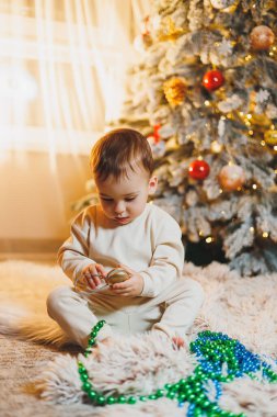 1 yaşında, Noel ağacının yanında, ağacın altında, yerde oturan tatlı bir çocuk. Tatil sezonu. Yeni yıl. Noel.