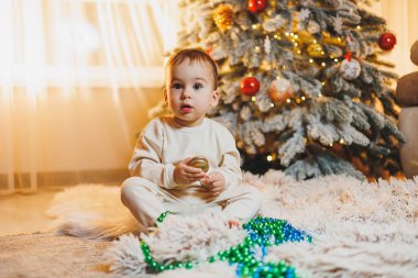 1 yaşında, Noel ağacının yanında, ağacın altında, yerde oturan tatlı bir çocuk. Tatil sezonu. Yeni yıl. Noel.