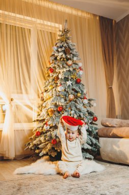 1 yaşında, Noel ağacının yanında, ağacın altında, yerde oturan tatlı bir çocuk. Tatil sezonu. Yeni yıl. Noel.