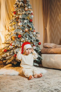 1 yaşında, Noel ağacının yanında, ağacın altında, yerde oturan tatlı bir çocuk. Tatil sezonu. Yeni yıl. Noel.