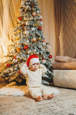 Noel Baba şapkalı, Noel ağacı olan şirin bir çocuk. Çocuklar için yeni yıl. Noel ağacı. Evde Noel atmosferi.