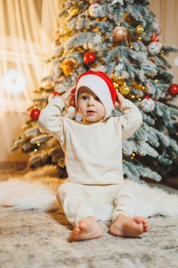 Noel Baba şapkalı, Noel ağacı olan şirin bir çocuk. Çocuklar için yeni yıl. Noel ağacı. Evde Noel atmosferi.