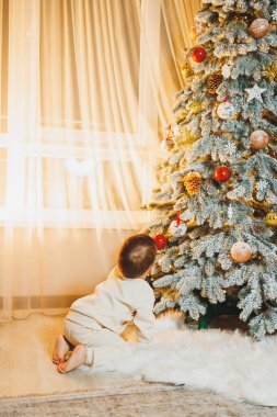 Noel Baba şapkalı, Noel ağacı olan şirin bir çocuk. Çocuklar için yeni yıl. Noel ağacı. Evde Noel atmosferi.