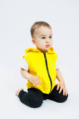 Beyaz arka planda sarı yelekli, neşeli bir çocuk. Çocukların parlak kıyafetleri. Kapüşonlu neşeli bir çocuğun portresi