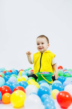Çocuk oyun grubunda renkli toplar içinde mutlu bir çocuk. Çocuk gülümsüyor, topların arasında saklanıyor..